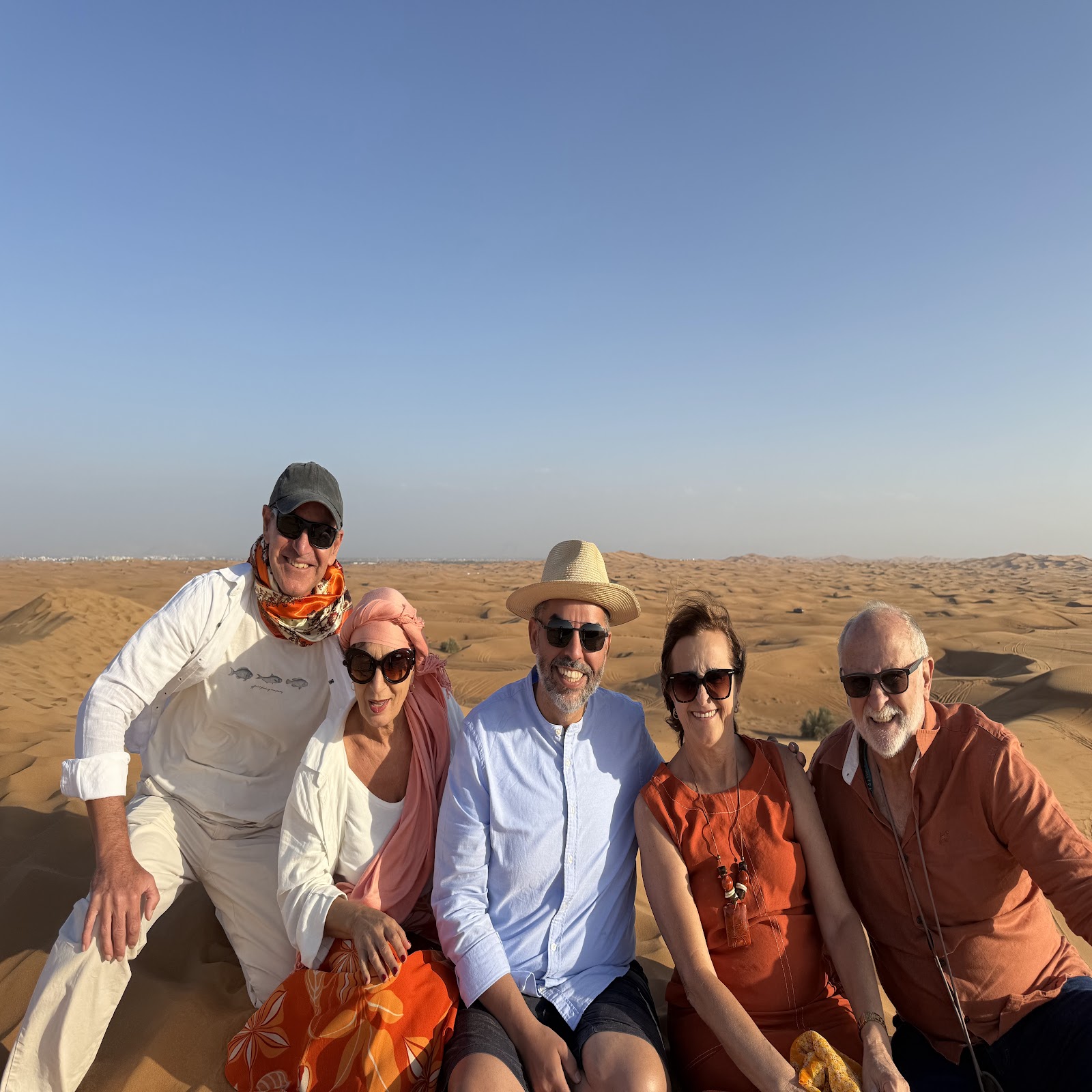 Grupo Rigue sentado nas dunas durante a experiência no deserto de Dubai